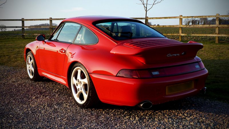 Rear three quarter of the waxed Porsche 993 Carrera 4S beside a fence line