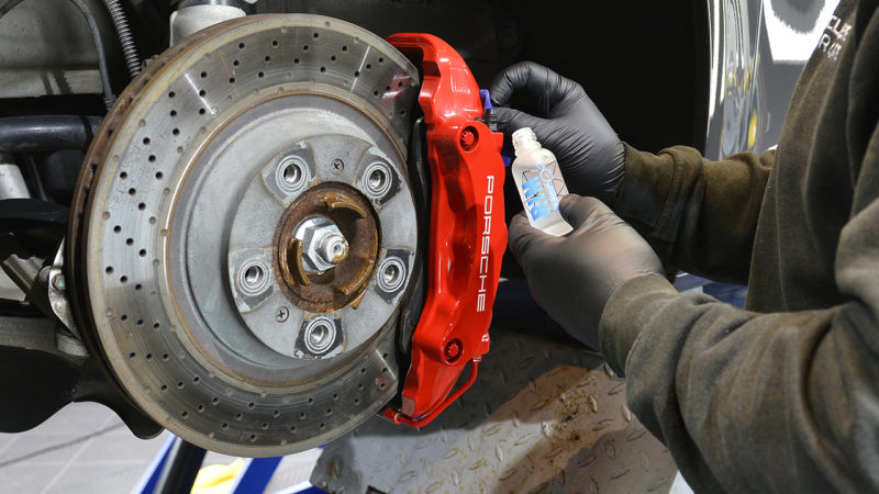 Red Porsche brake caliper being cleaned and sealed with the wheel off the car